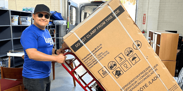 Lugg delivery professional smiling while using a dolly to move a boxed appliance for same-day delivery.
