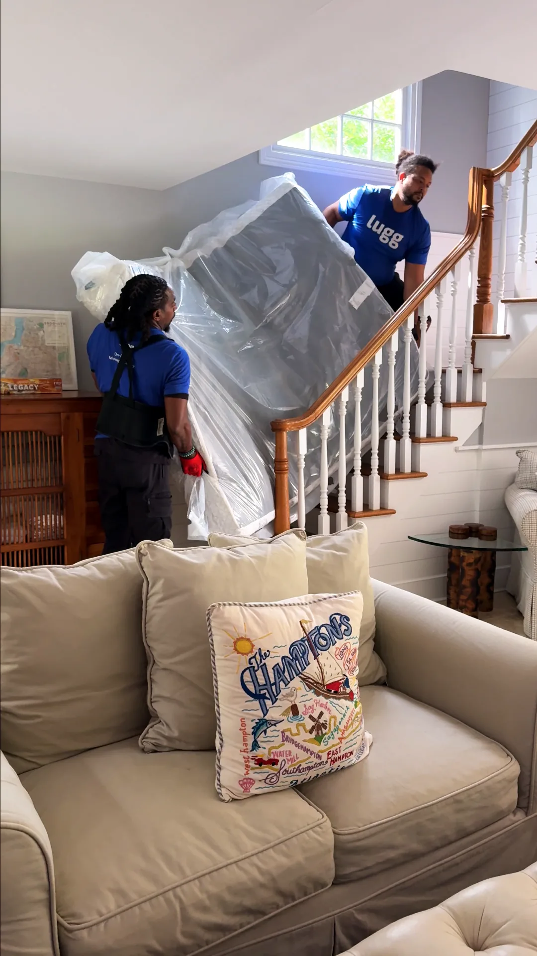 Two Luggers carrying a wrapped mattress up a staircase