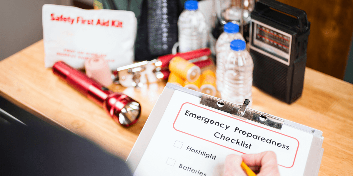 Emergency preparedness checklist with flashlight, first aid kit, and water bottles on a table.