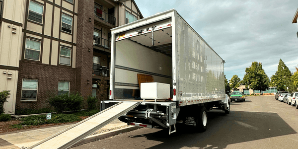 A large moving truck parked outside an apartment complex with its ramp down, ready for loading furniture and boxes on moving day.