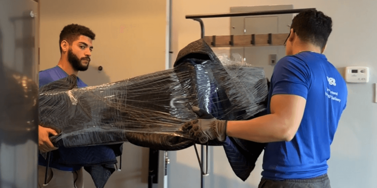 Lugg movers carrying wrapped furniture into a student’s dorm room during move-in.