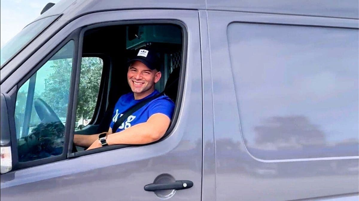 Lugg driver smiling behind the wheel of a sprinter van heading to a job