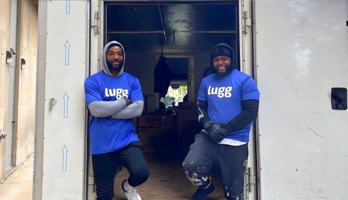 Two Lugg movers in branded blue shirts posing confidently at the back of a box truck