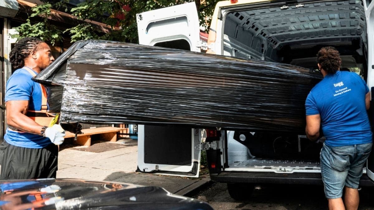 Two Lugg movers loading shrink-wrapped furniture into a delivery van