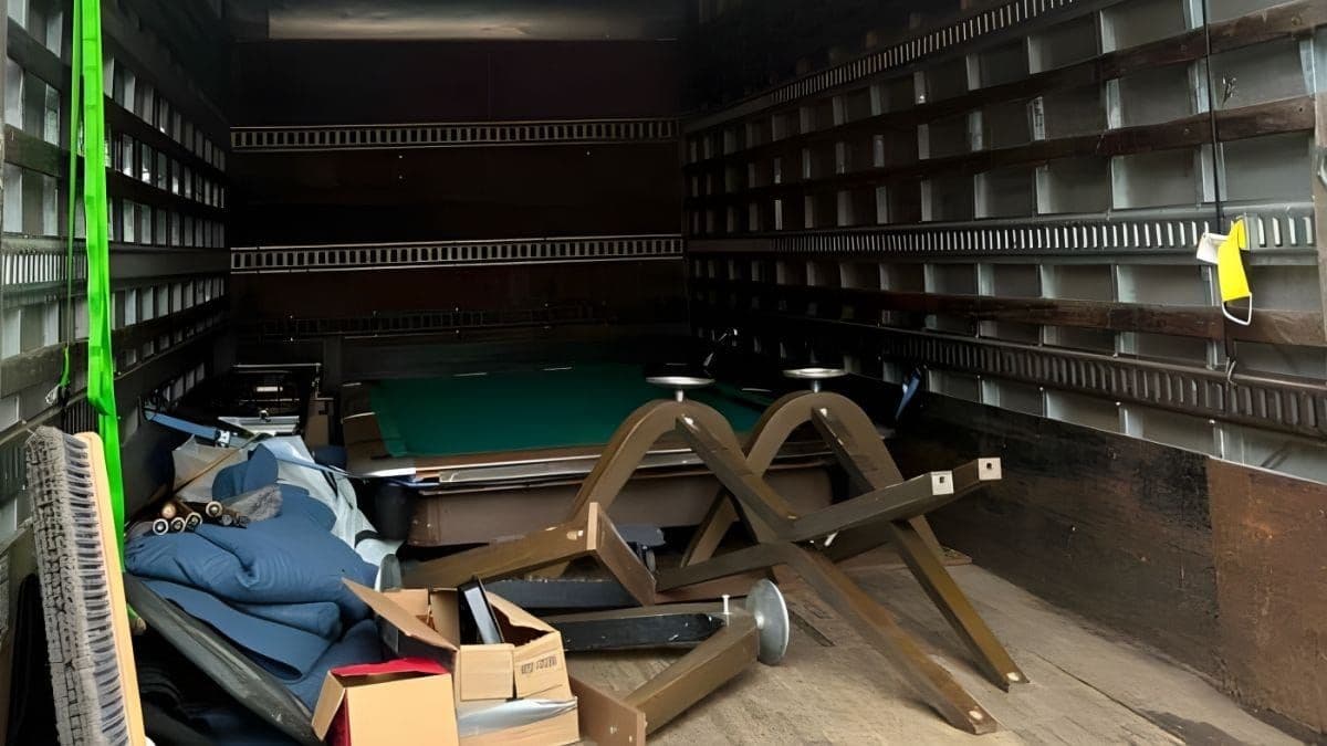 Disassembled pool table loaded in a Lugg moving truck, with slate slabs flat on the floor and wooden legs strapped beside them