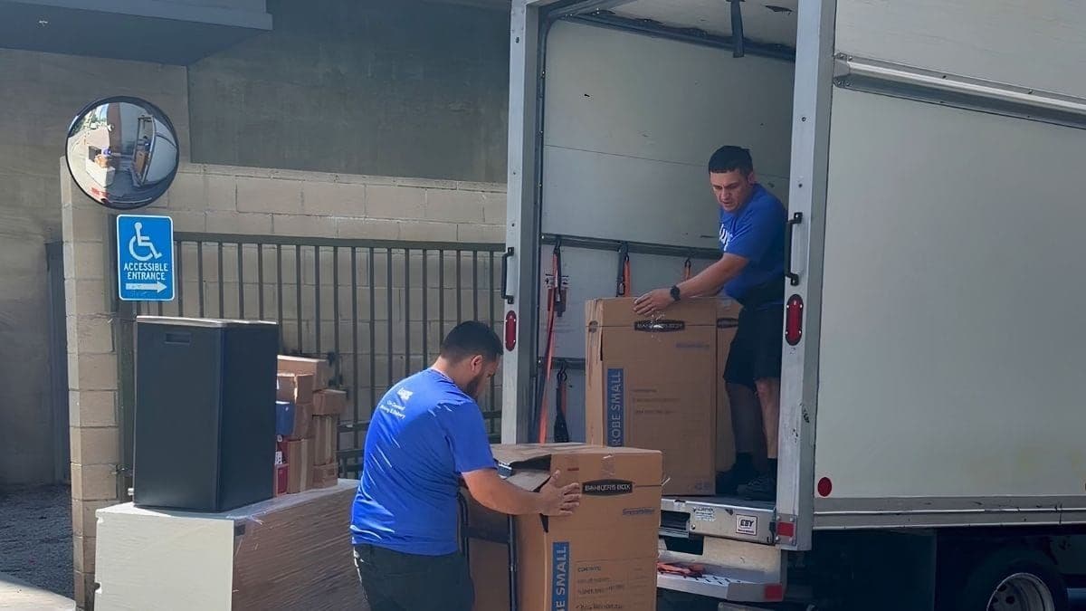 A Lugg 2-Lugger crew loads wardrobe boxes into a box truck — a typical on-demand box truck driver job in a city loading dock.