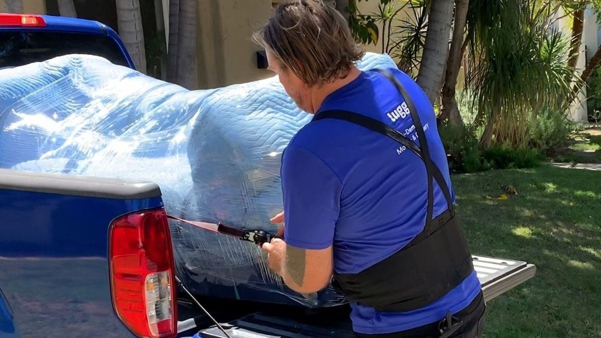 Lugg driver strapping a wrapped load in a pickup truck on a sunny day — on-demand moving is one of the highest paying summer jobs.