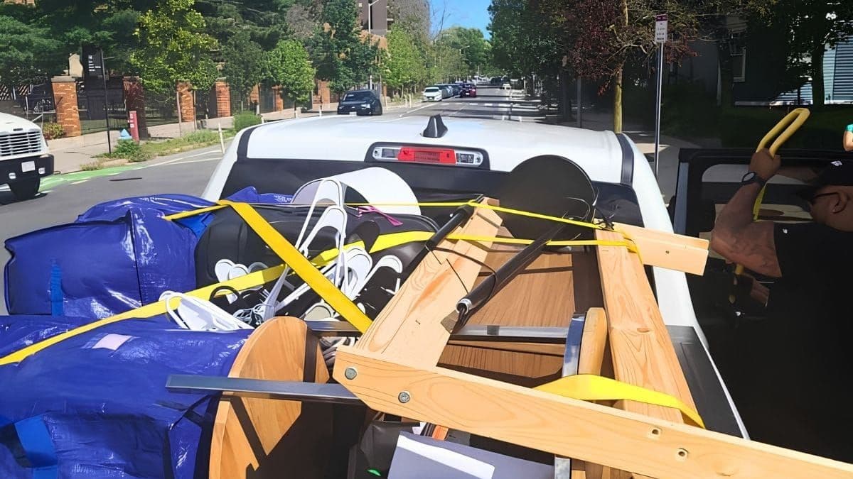 Pickup truck packed with luggage, bags, and furniture under yellow straps on a tree-lined Boston street during Allston Christmas move-out day