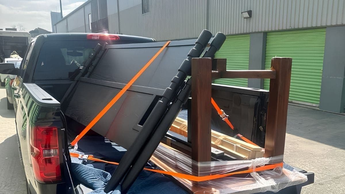 Plastic-wrapped, strapped furniture loaded on a pickup truck parked outside green storage units for short-term storage