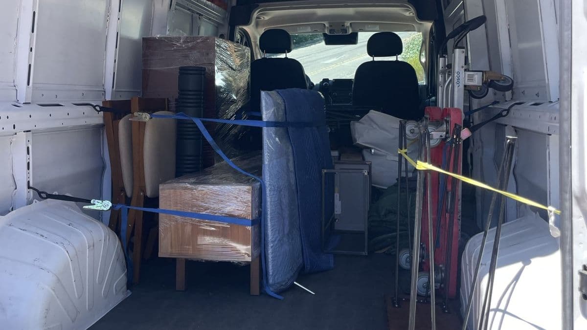Furniture wrapped in moving blankets and ratchet-strapped inside a Lugg cargo van, with hand trucks secured alongside
