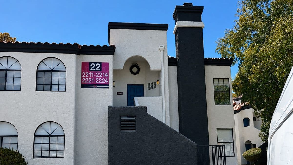 Cream stucco apartment building in Las Vegas with a tile roof, arched windows and an exterior staircase to a second-floor unit, surrounded by desert rock landscaping.
