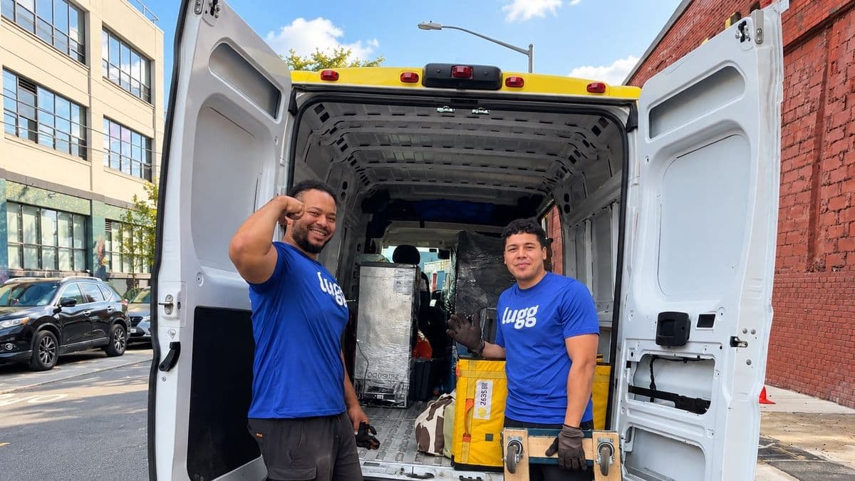 Two Luggers stand beside an open cargo van with moving equipment on a city street on a weekend morning.