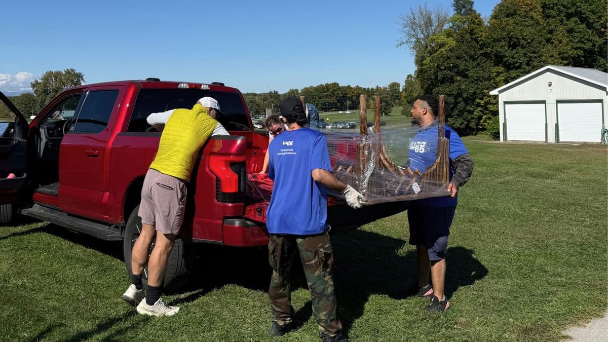 Lugg movers loading wrapped antique furniture into a pickup truck at an outdoor antiques fair.