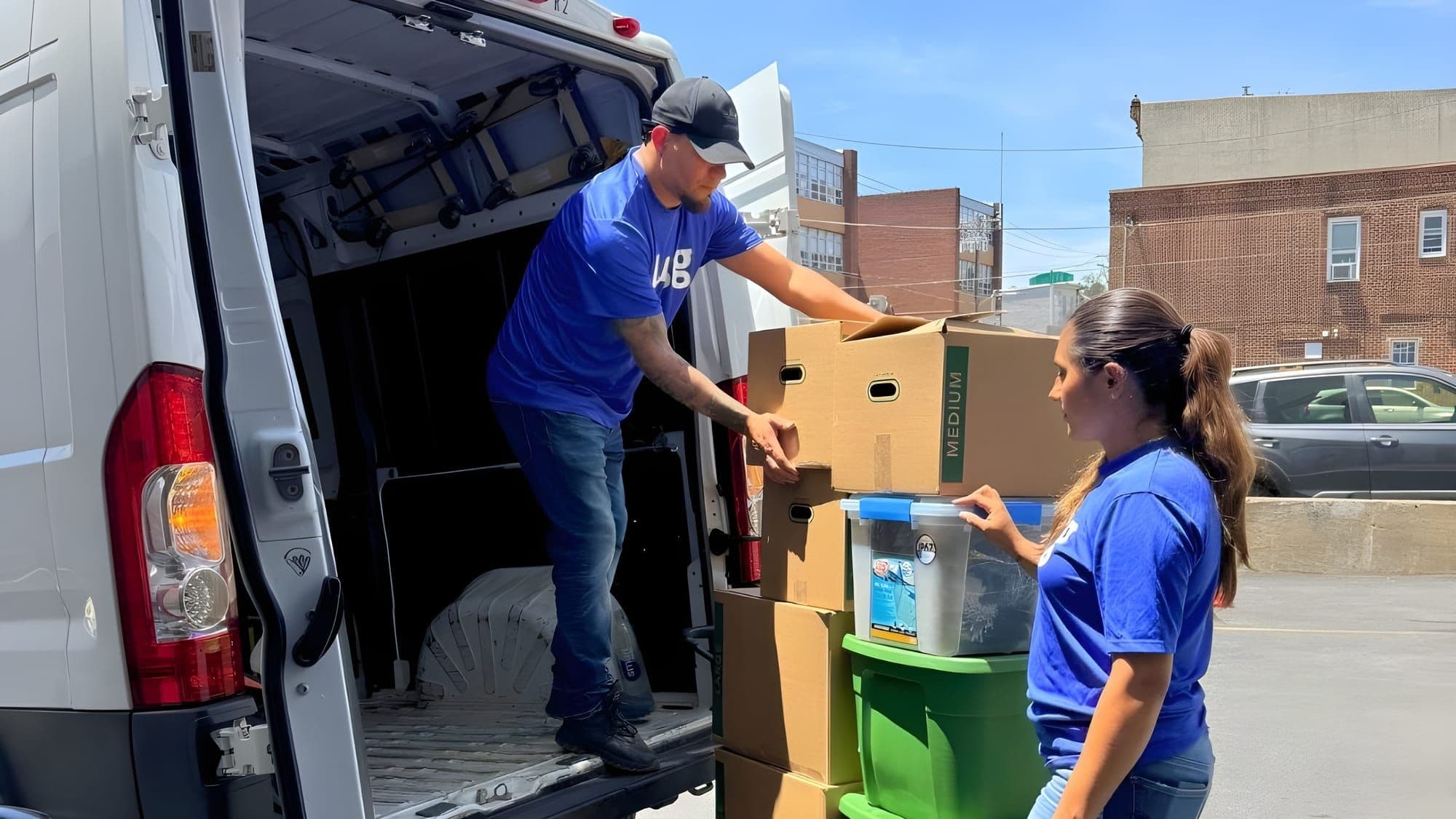 Two Lugg movers in branded blue tees load moving boxes into a cargo van on a sunny day, a flexible summer job for teachers.