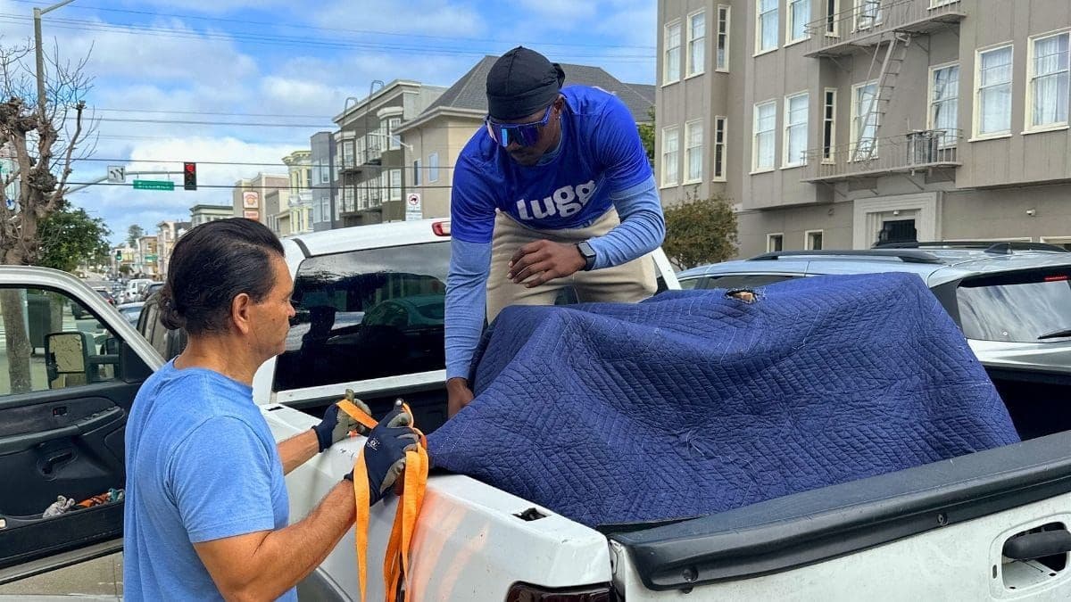 Two Luggers load a moving-blanket-wrapped item into a personal pickup truck — making extra money with a vehicle they own.