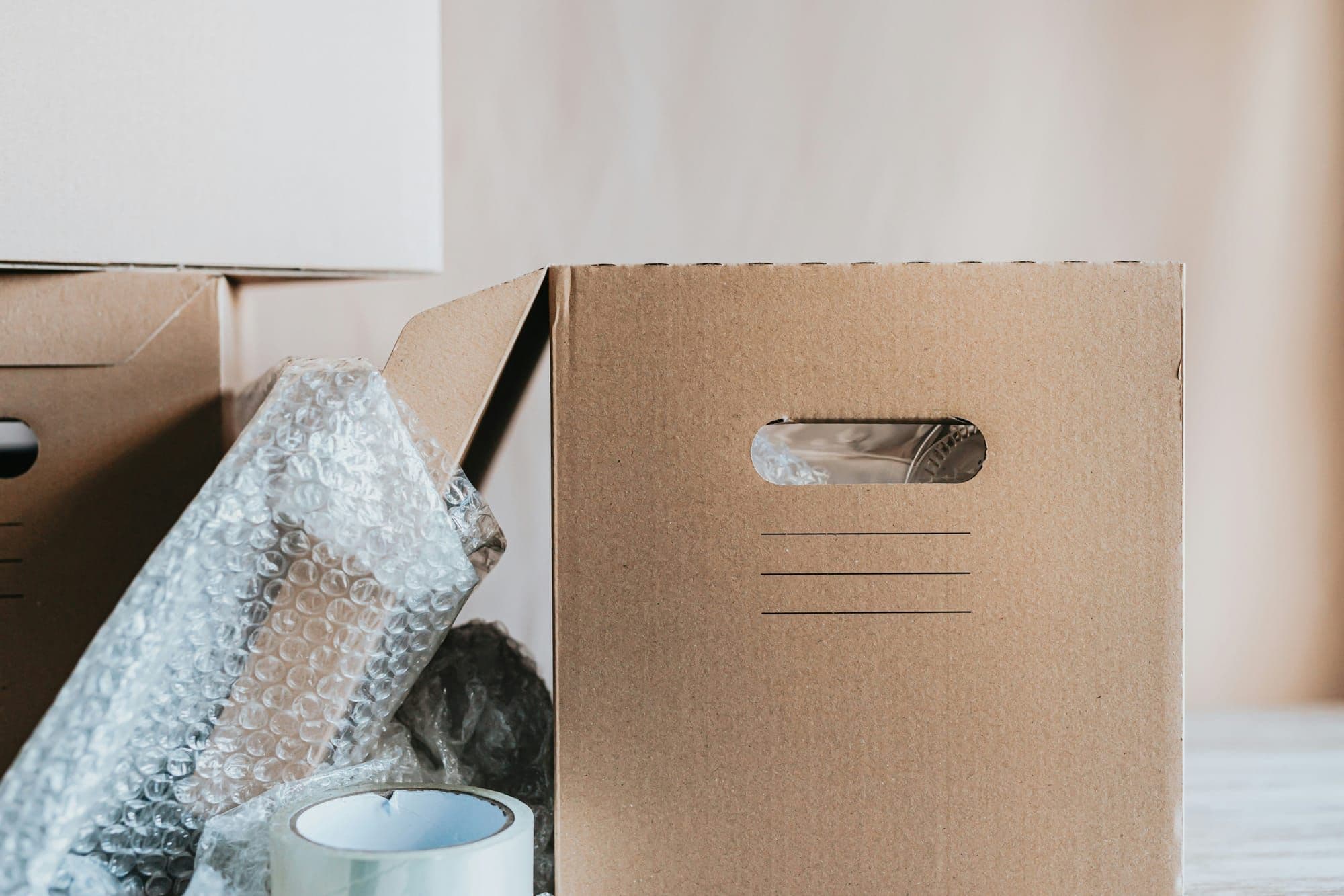 A moving box with a handle next to bubble wrap and a roll of packing tape — essential packing supplies for a move