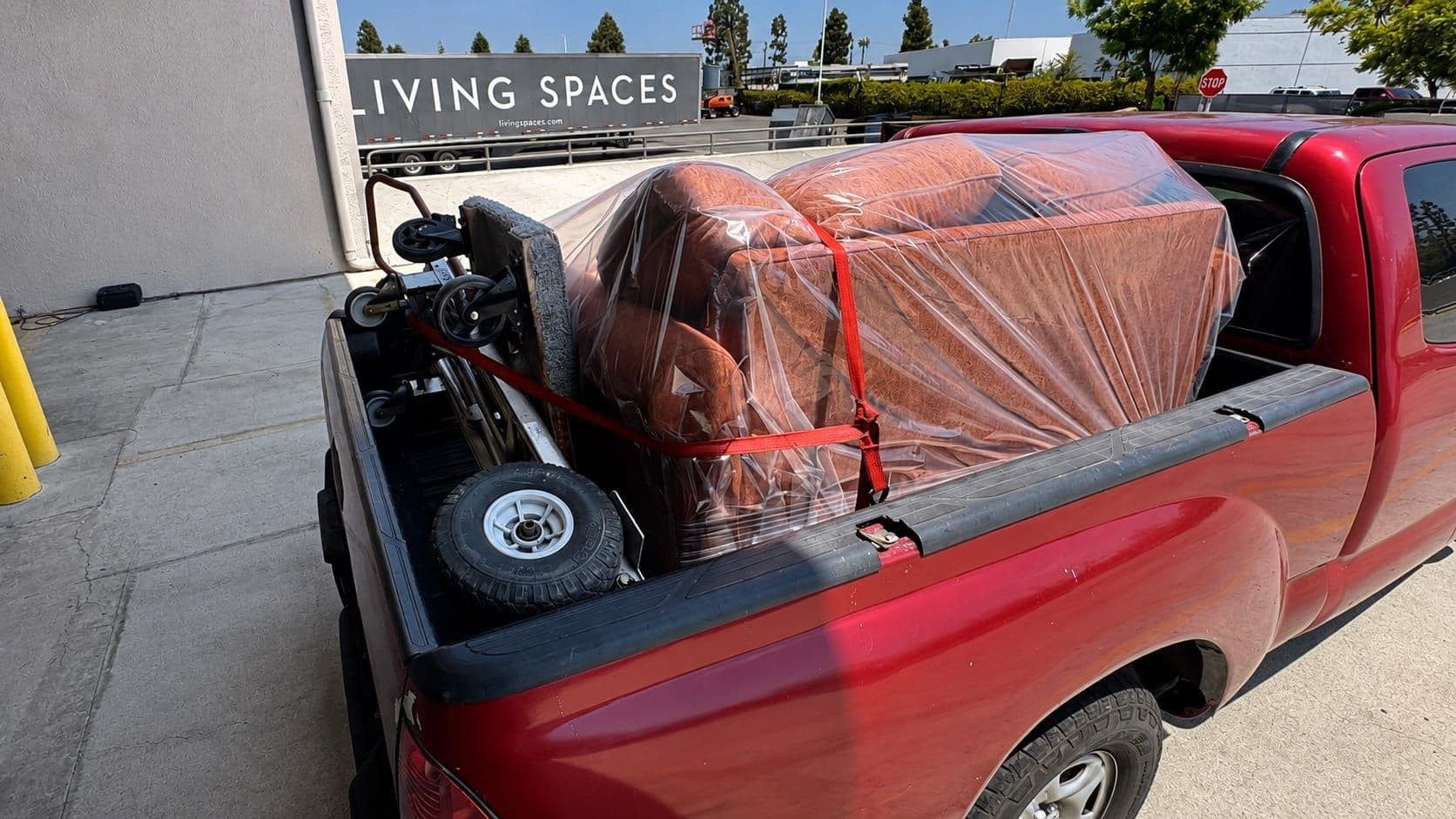 A red pickup truck loaded with a shrink-wrapped armchair outside the Living Spaces customer pickup bay