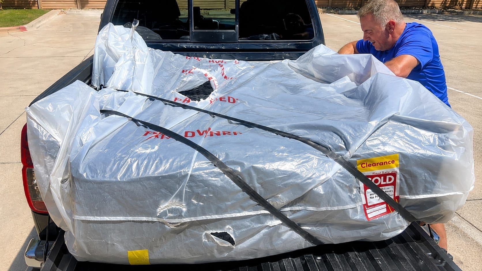 A mattress with a clearance sticker loaded in the bed of a pickup truck outside a furniture store during a Labor Day sale