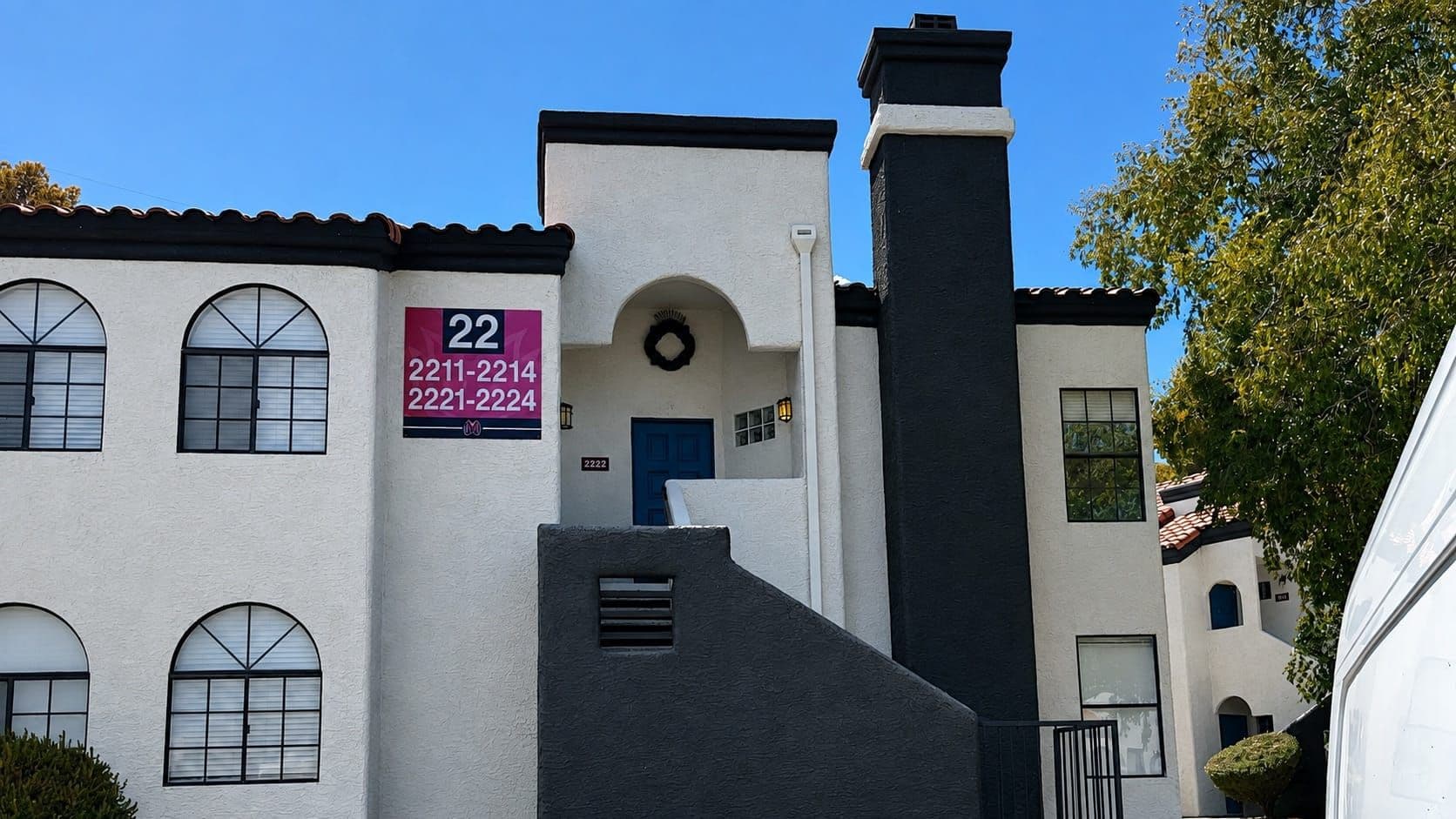 Cream stucco apartment building in Las Vegas with a tile roof, arched windows and an exterior staircase to a second-floor unit, surrounded by desert rock landscaping.