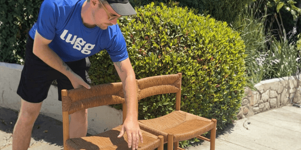 A mover in a blue Lugg shirt lifting two Charlotte Perriand Dordogne chairs outdoors, illustrating safe and simple local delivery for high-quality used furniture.