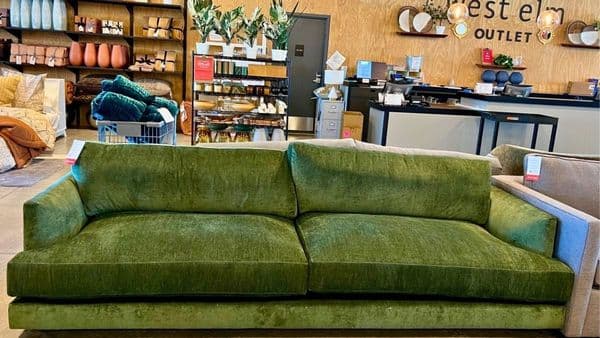 Green velvet sofa on sale at a West Elm Outlet with 50% off clearance signs in the background