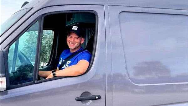 Lugg driver smiling behind the wheel of a sprinter van heading to a job