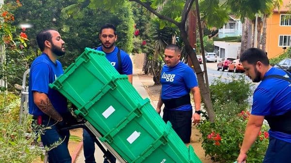 Lugg movers carrying stacked green reusable plastic bins on a dolly — an eco-friendly moving alternative to cardboard boxes