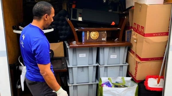 A Lugg mover in branded blue gear loading a packed moving truck with bins, boxes, and furniture during a college move-out