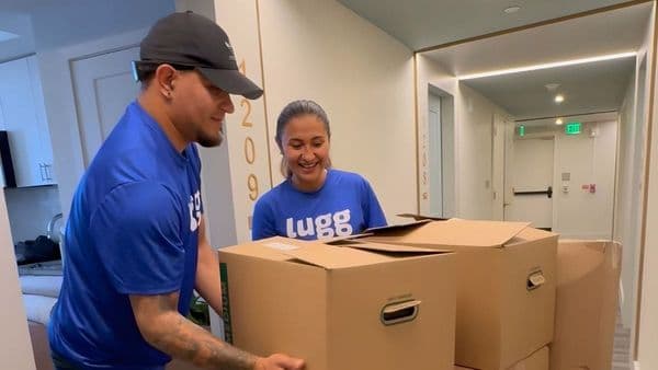 Two Lugg movers in branded blue shirts handling moving boxes in an apartment hallway during a college move-out