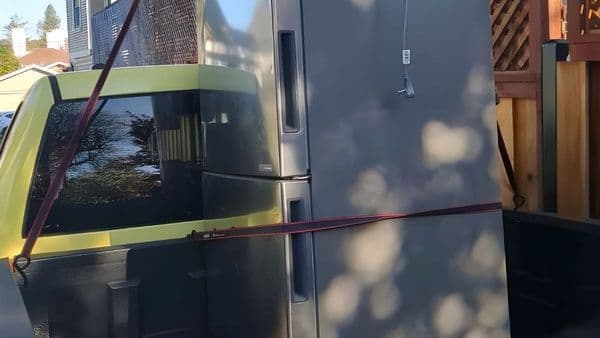 Stainless steel French-door refrigerator secured upright in a pickup truck bed with ratchet straps